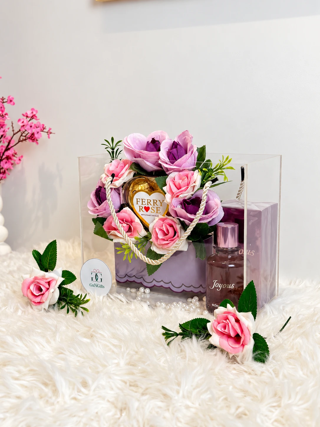 A clear acrylic gift bag of pink and lilac roses with Ferry Rose chocolates and a Joyous perfume